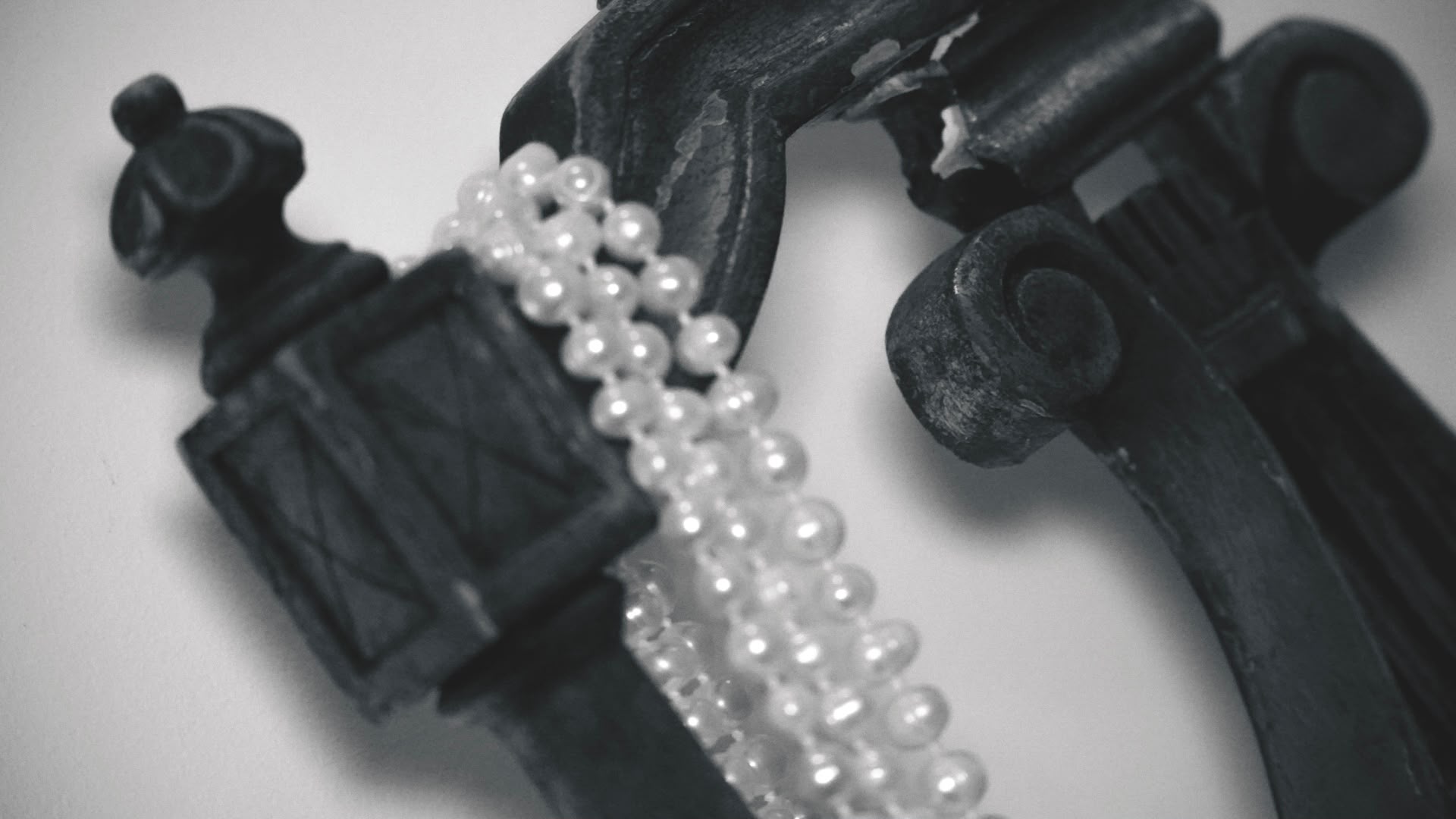 Zwart-wit detail van een parelketting over klassiek smeedwerk